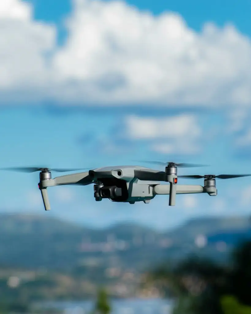 High-tech drone in flight with a clear blue sky and clouds in the background, showcasing technology and innovation.